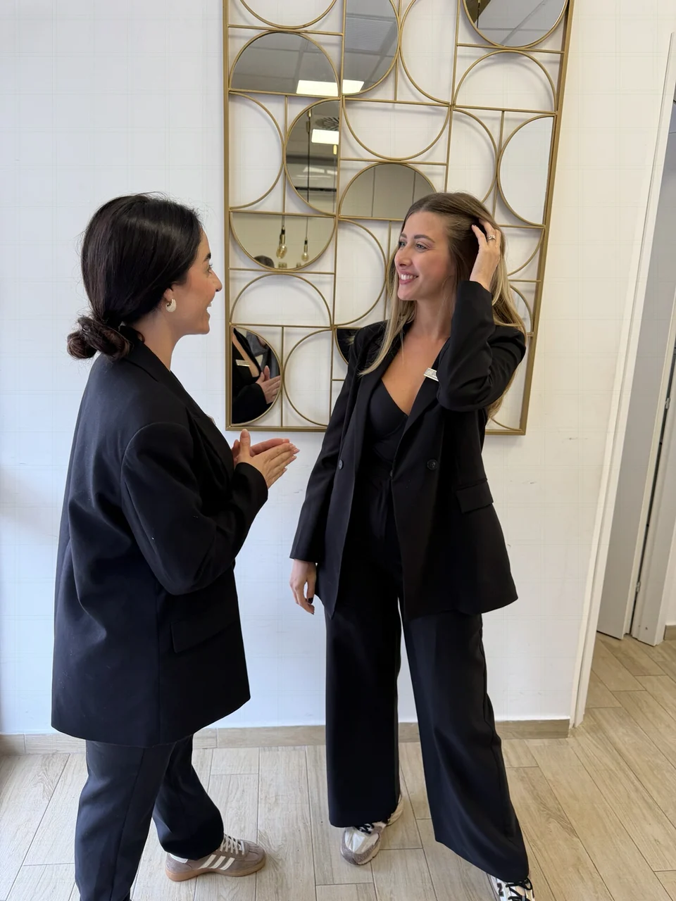 Giada e Luana insieme in abiti neri, sorridenti davanti allo specchio geometrico dorato del centro GL
